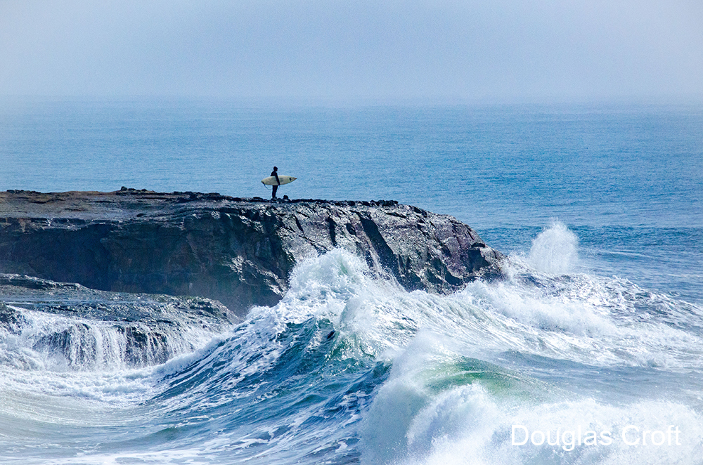 a surfer standing on a cliff above waves
