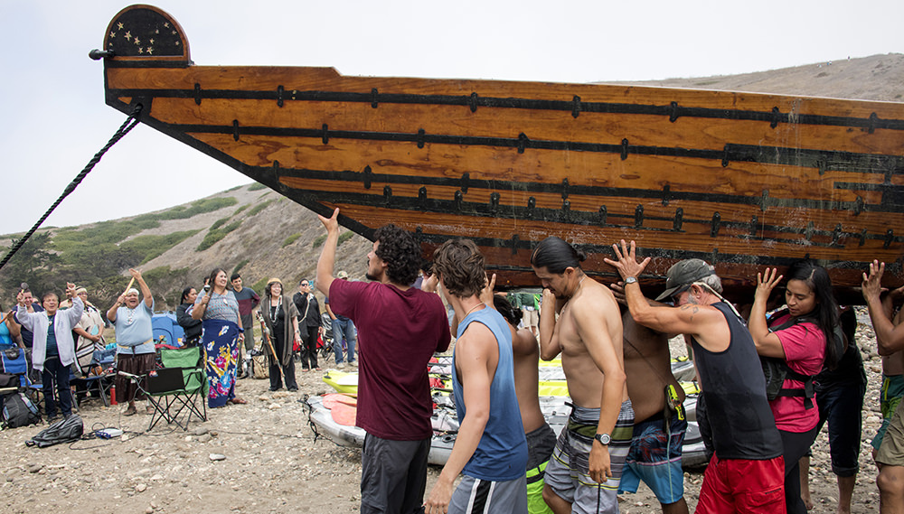 crew members carry the tomol on shore