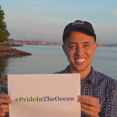 person near the ocean holding a sign that says #PrideInTheOcean