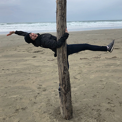 a person with arm and leg outstretched while holding onto a driftwood pole