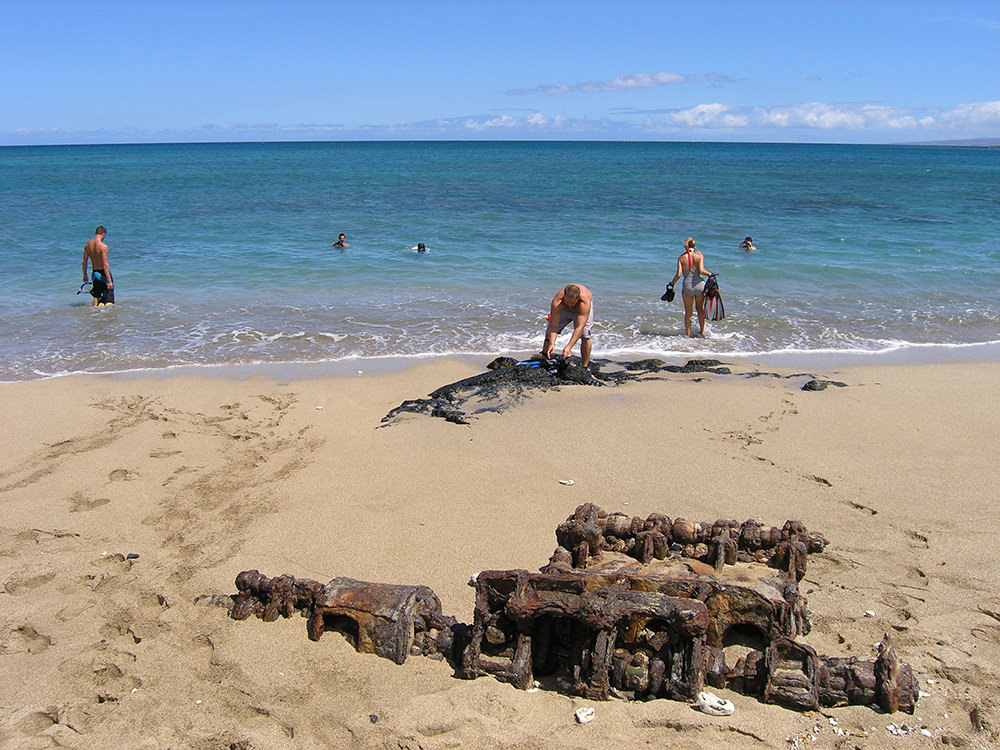 people on a beach near rusted engine parts