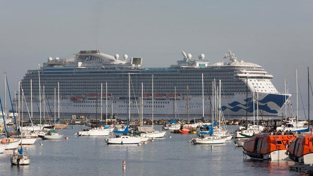 a cruise ship in port behind sailboats
