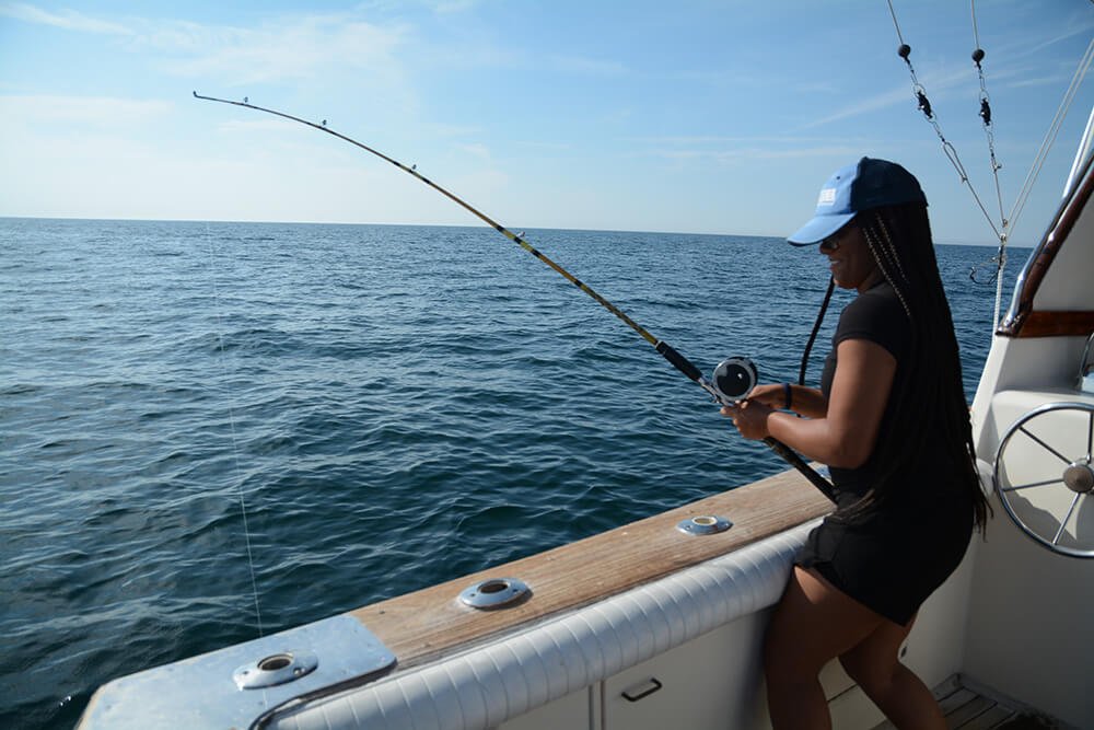 Recreational fisher reels in a catch from the deck of a charter fishing boat.