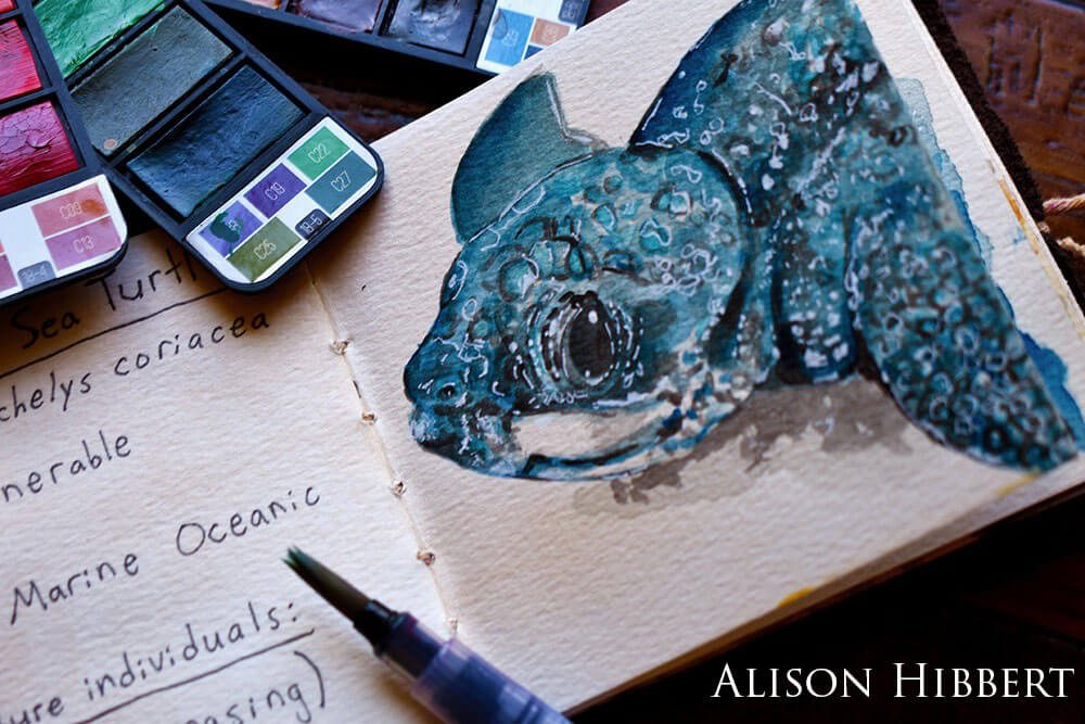A watercolor painting of a leatherback sea turtle next in a journal next to some paint palettes.