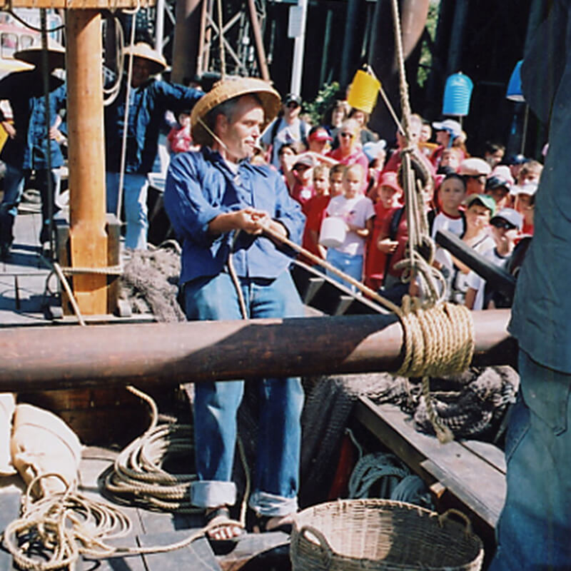 a person leaning back while holding a rope attached to vessel in front of a group of children
