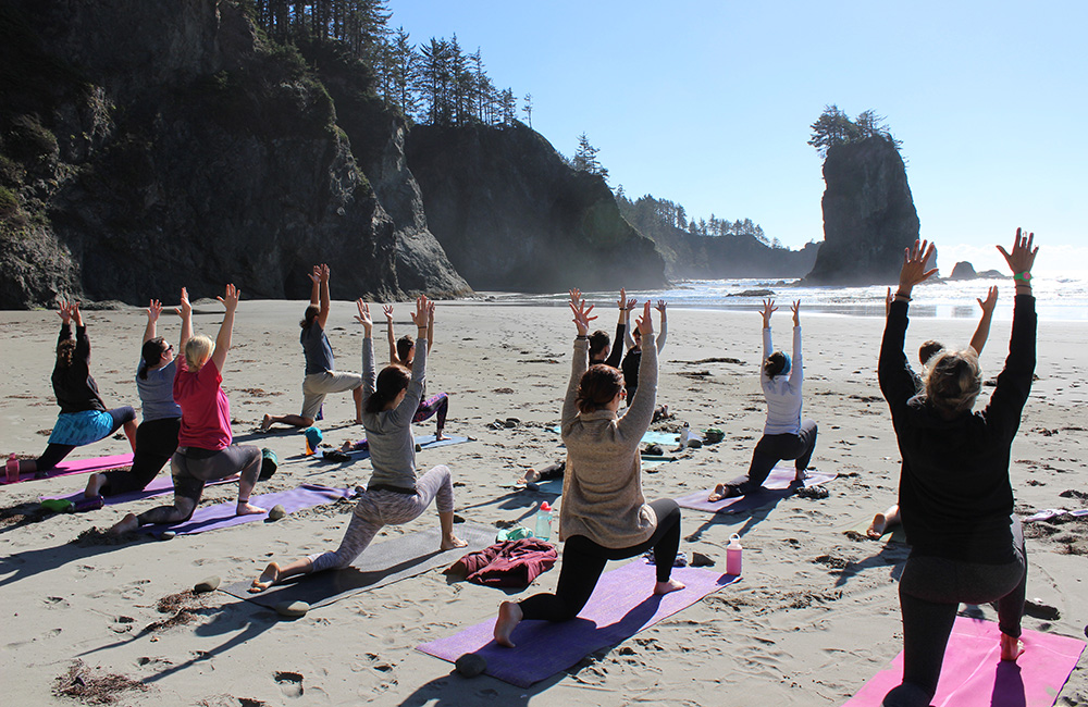A group of people do stretches on yoga mats on a beach