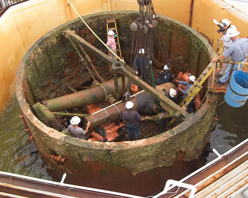 aerial view of workers standing inside of the turret performing preservation work. The two cannons can be seen from above