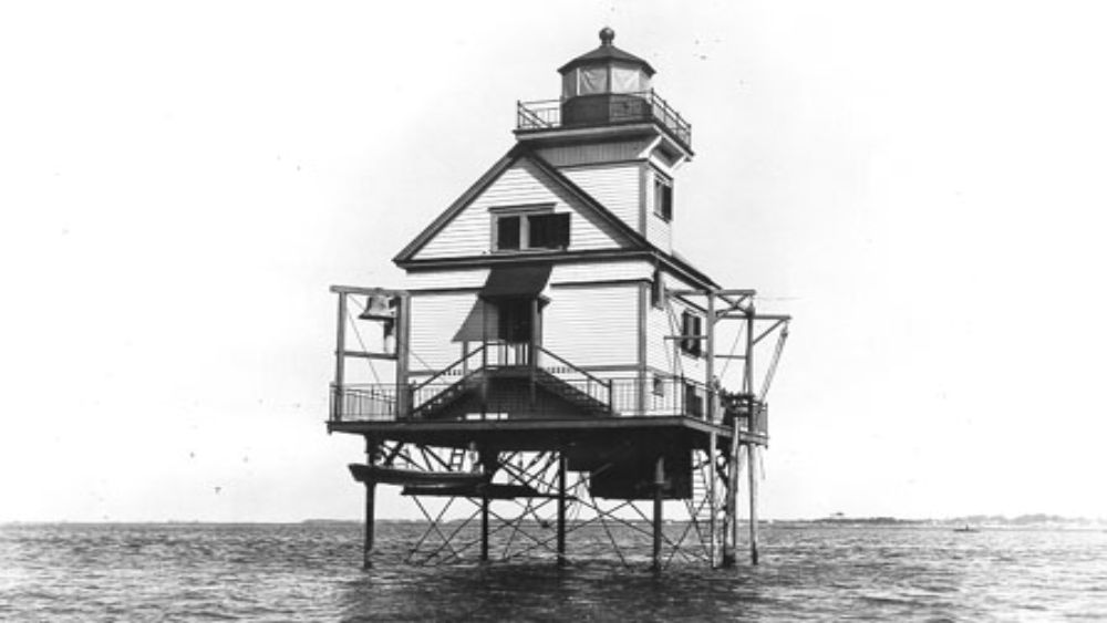 a lighthouse and keeper's house sit in stilts offshore of a low sandy island
