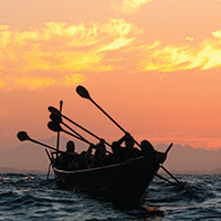 Tomol pullers paddling in front of a sunrise