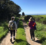 beth cataldo and holly reed walking along a trail near the coast