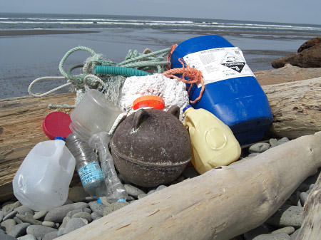 collected marine debris piled up on the beach, including water bottles, milk jugs, derelict fishing gear and hazardous material containers